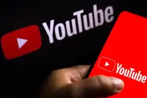 Imagem de uma mão acessando o Youtube no celular e no fundo a logo do Youtube. 